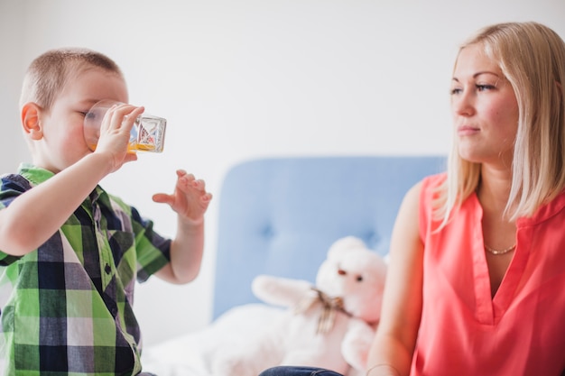 Frau schaut ihren Sohn beim trinken einen Saft