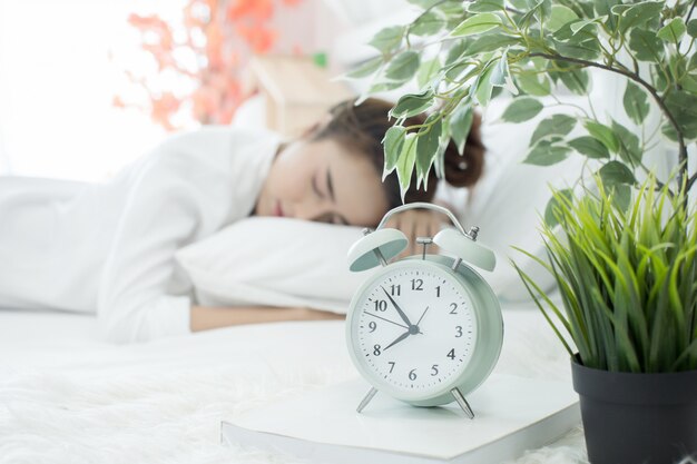 Frau schläft im Bett, während ihr Wecker die frühe Zeit zu Hause im Schlafzimmer zeigt