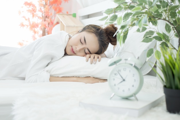Frau schläft im Bett, während ihr Wecker die frühe Zeit zu Hause im Schlafzimmer zeigt