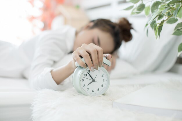 Frau schläft im Bett, während ihr Wecker die frühe Zeit zu Hause im Schlafzimmer zeigt