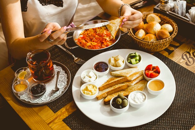 Frau schmiert Butter auf Toast vom Frühstückssatzei mit Tomatenbutterhonigolivenkäse-Tomaten-Gurkentee-Zitronenmarmeladen-Seitenansicht