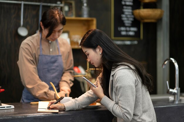 Frau schreibt auf einem Notizbuch, während Mann in einem Restaurant kocht