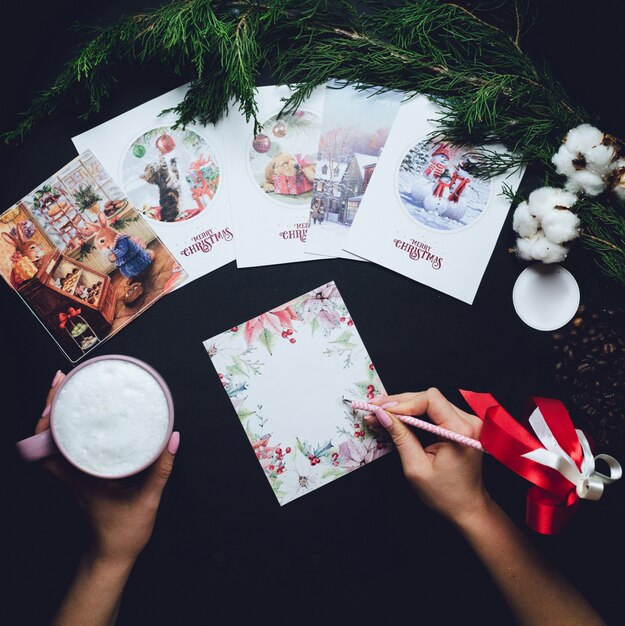 Frau schreibt etwas auf Weihnachtspostkarte mit einer Tasse Milch