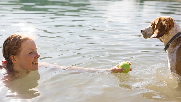 Frau schwimmt und spielt mit Hundeseitenansicht
