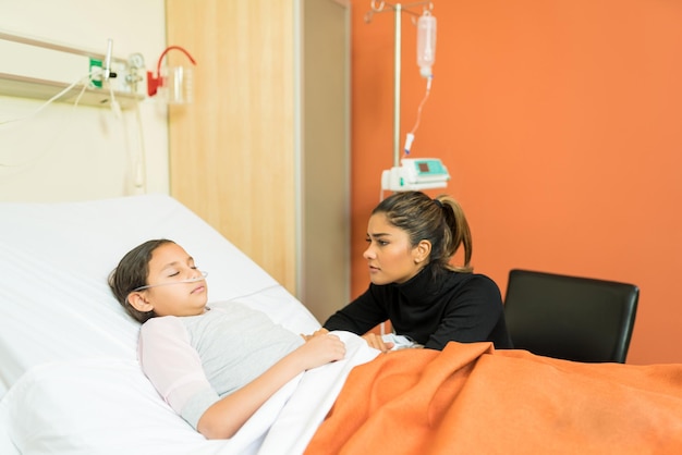 Frau sieht bewusstlose Tochter an, während sie im Krankenhaus am Bett sitzt