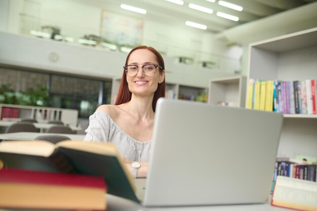 Frau sitzt am Tisch mit Laptop und schaut in die Kamera