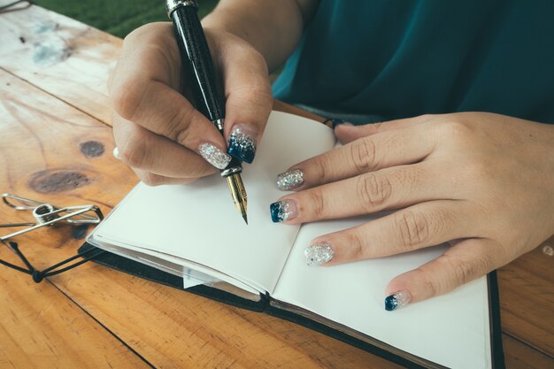 Frau sitzt am Tisch und schreibt im Notizbuch in schönem Licht Heimat Innenraum. Zuhause arbeiten. Freiberufler. Ideen schreiben. drinnen. Vintage gefiltertes Bild.