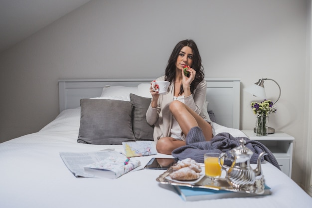 Frau sitzt auf dem Bett mit einer Erdbeere in der Hand