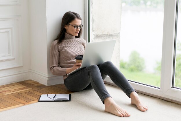 Frau sitzt auf dem Boden und arbeitet an ihrem Laptop