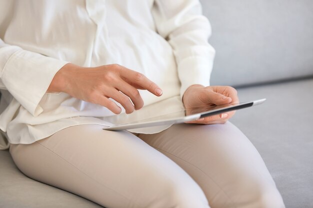 Frau sitzt auf der Couch und benutzt Tablette