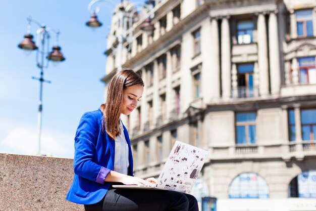 Frau sitzt auf der Straße und arbeitet mit einem Laptop