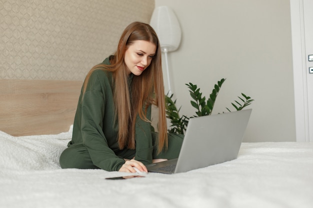 Frau sitzt auf einem Bett und benutzt einen Laptop