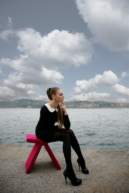 Frau sitzt auf einem rosa Stuhl am Strand