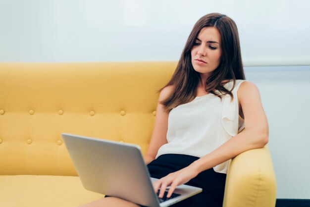 Frau sitzt auf einem Sofa mit einem Laptop auf den Beinen