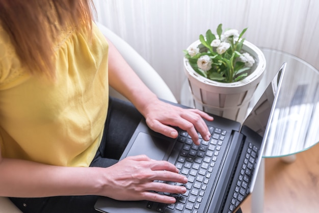 Frau sitzt auf einem Stuhl mit einem Laptop auf dem Schoß