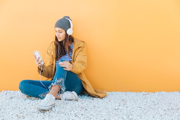 Frau sitzt auf Teppich mit Smartphone Musik über Kopfhörer hören