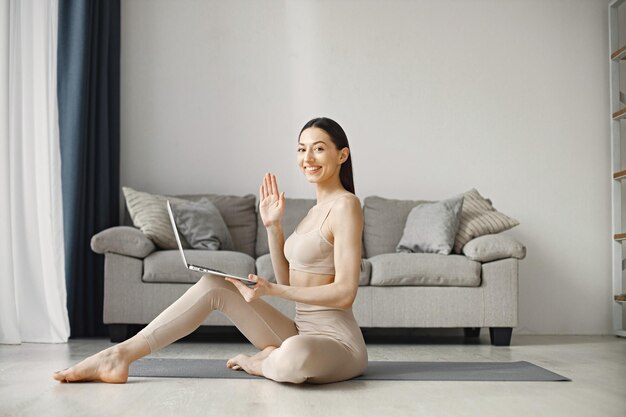 Frau sitzt auf Yoga-Mann in Leggins und Top, während sie zu Hause auf dem Laptop arbeitet