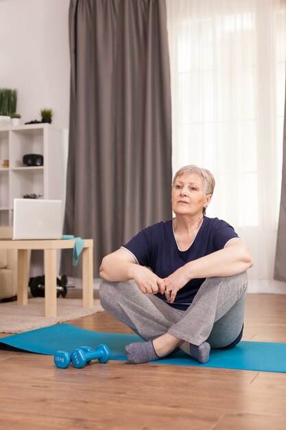 Frau sitzt auf Yogamatte und wartet auf den Wellnesstrainer
