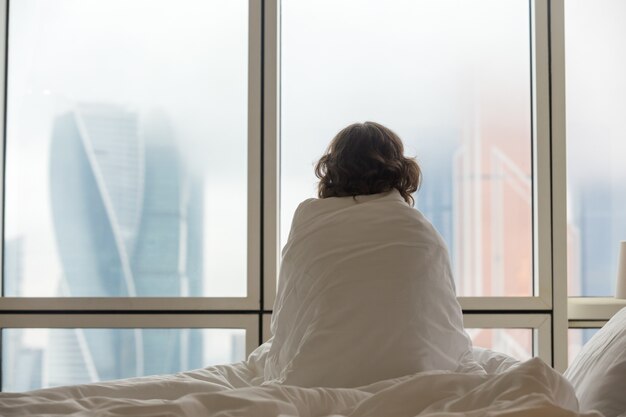 Frau sitzt im Bett sucht durch das Fenster