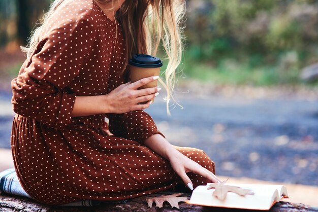 Frau sitzt mit einer Tasse Kaffee und Büchern im Freien