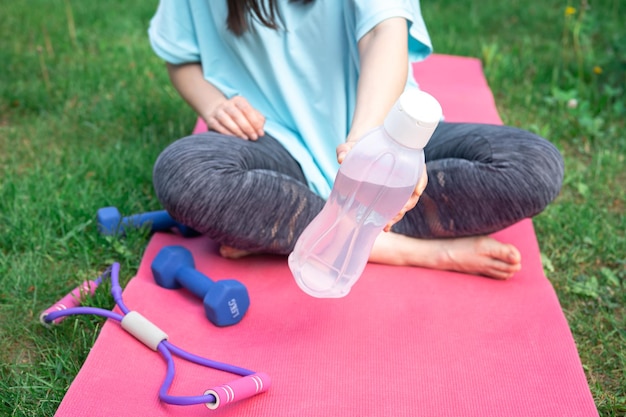 Kostenloses Foto frau sitzt nach dem training auf der matte, wasserflasche aus nächster nähe