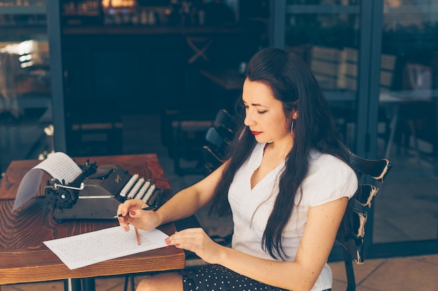 Frau sitzt und schreibt auf Papier in der Caféterrasse im weißen Hemd während des Tages