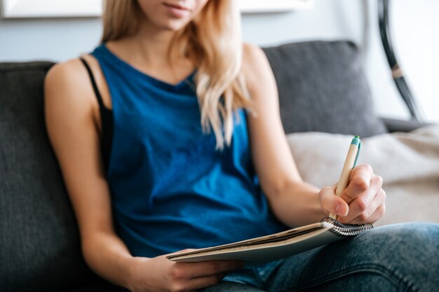 Frau sitzt und schreibt im Notizblock zu Hause