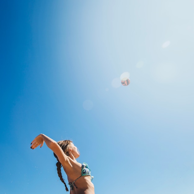 Frau spielt Beach-Volley mit Sonne im Hintergrund