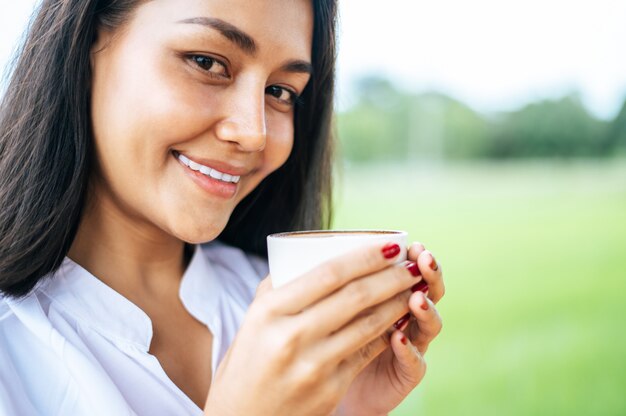 Frau stand glücklich und trank Kaffee auf der Wiese