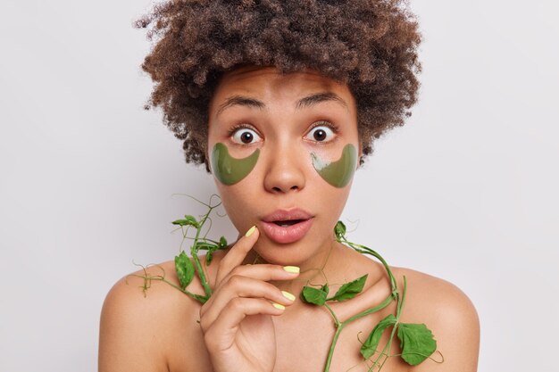 Frau starrt beeindruckt in die Kamera trägt grüne Hydrogel-Pflaster auf verwendet grüne Erbsenpflanze, die feuchtigkeitsspendende und glättende Anti-Aging-Vorteile für Haut und Haar bietet