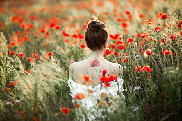 Frau steht mit nacktem Rücken, es gibt eine Tattoo Blumenmohnblume, zwischen dem Mohnblumenfeld
