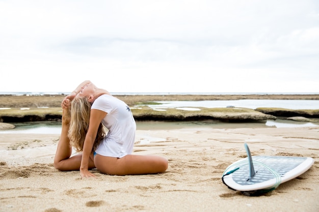 Frau Stretching Body von Surfboard am Strand