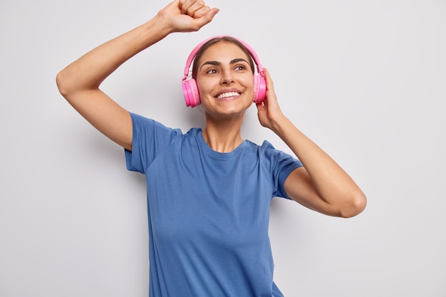 Frau tanzt im Rhythmus der Musik fängt jedes Stück des Liedes trägt drahtlose Kopfhörer in einem lässigen blauen T-Shirt auf Weiß gekleidet