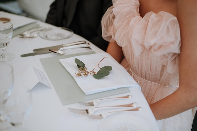 Frau trägt ein Kleid, das vor einem Hochzeitstisch mit einer Serviette und einem grünen Blatt darauf sitzt