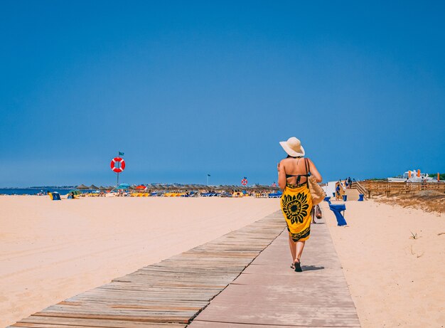 Frau trägt einen Bikini und einen Hut zu Fuß am Strand