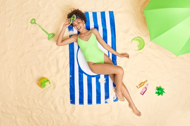 Frau trägt grünen Bikini und Schnorchelbrille liegt auf blau gestreiftem Handtuch genießt den Sommerurlaub verbringt Freizeit am Sandstrand Sonnenbaden während des sonnigen Tages. Ferien.
