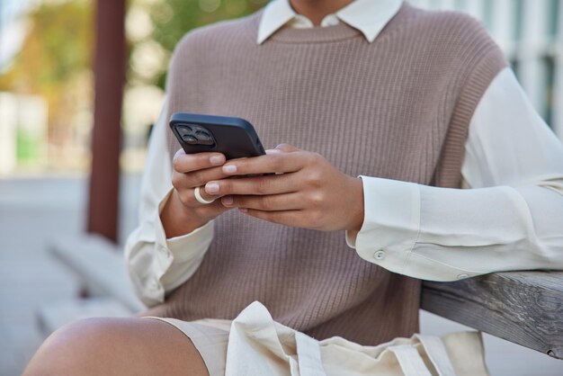 Frau trägt ordentliche Kleidung benutzt Handy sendet Textnachrichten und E-Mails Chats onlie sitzt auf Holzbank