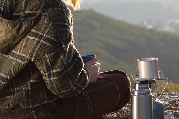 Frau trägt Sweatshirt und trinkt Tee auf dem Gipfel des Berges