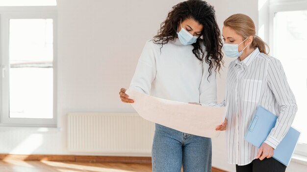 Frau und Makler, die Hauspläne zusammen betrachten, während sie medizinische Masken tragen