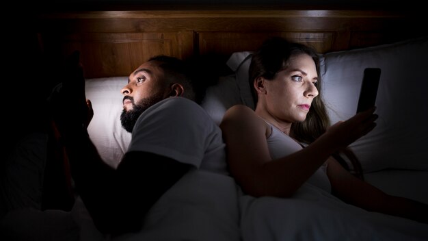 Frau und Mann überprüfen ihre Telefone vor dem Schlafen
