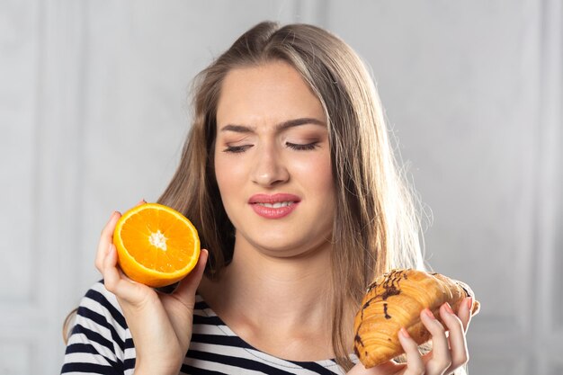Frau vergleicht ungesunden Kuchen und Orangenfrucht