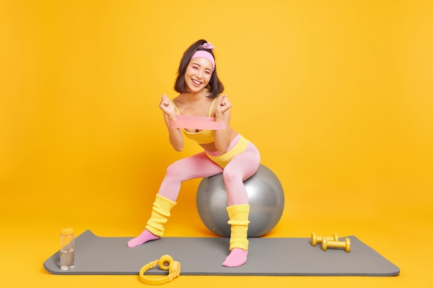 Frau verwendet Sportzubehör trainiert die Armmuskulatur mit Widerstandsband sitzt auf einem Fitnessball in Activewear