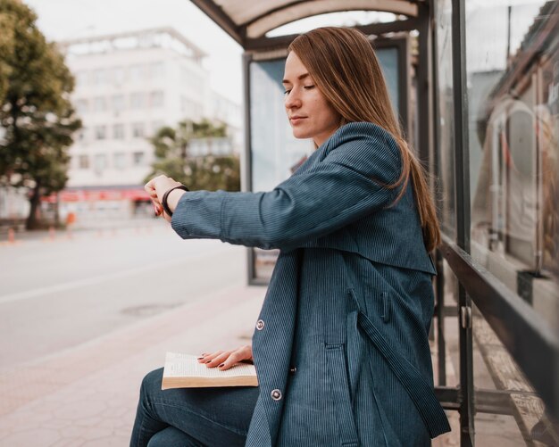 Frau wartet auf den Bus und sitzt mit einem Buch auf ihrem Schoß