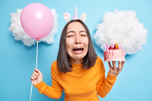 Frau weint aus Verzweiflung hält aufgeblasenen Ballon und leckeres Dessert hat am Geburtstag unglückliche Stimmung
