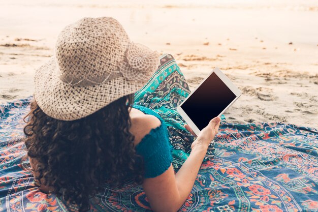 Frau, welche die Tablette liegt am Strand verwendet