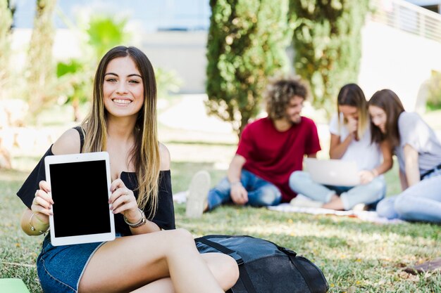 Frau, welche die Tablette sitzt auf Gras zeigt