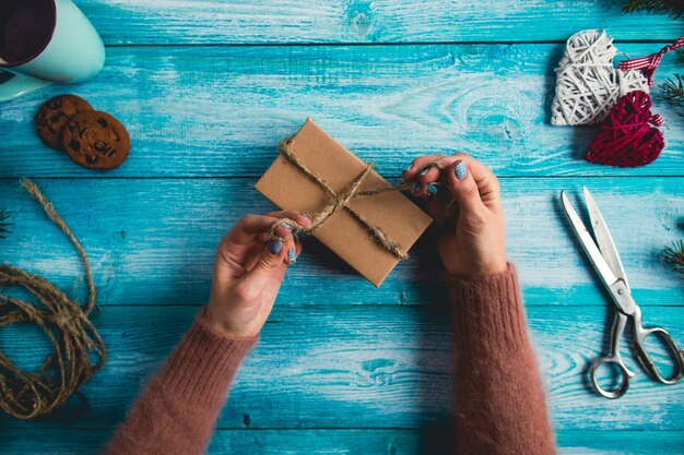 Frau wickelt Weihnachtsgeschenke auf blauem Holztisch ein