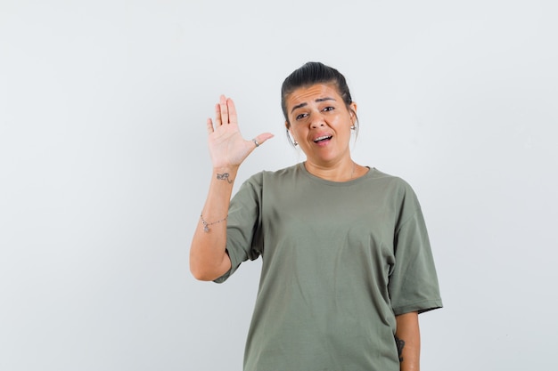 Frau winkt Hand für Begrüßung im T-Shirt und schaut selbstbewusst