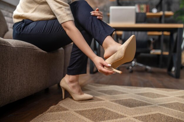Frau zieht stylische hochhackige Schuhe auf dem Teppich aus