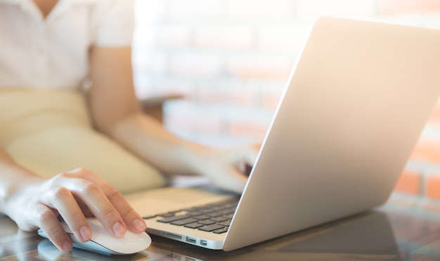 Frau zu berühren, eine Maus und schaut auf einen Laptop